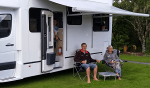 Keith and Brenda sitting outside their solar powered off-grid motorhome under the awning